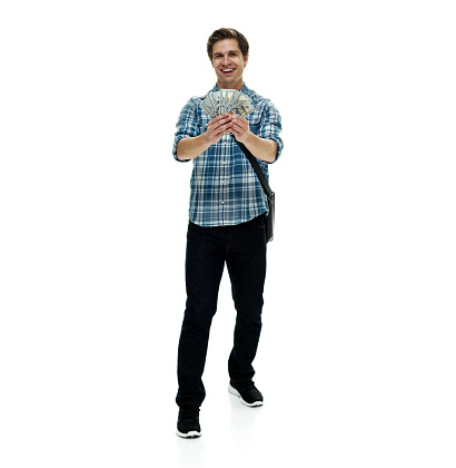 Full length of aged 20-29 years old with short hair caucasian young male standing in front of white background wearing shoulder bag who is laughing and holding us currency