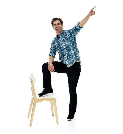 Front view of aged 20-29 years old with short hair caucasian young male standing in front of white background wearing sports shoe who is happy who is pointing