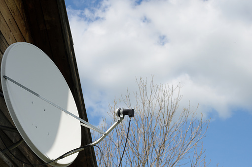 Satellite dish on a country house on a background of a blue sky with clouds. The importance of telecommunications in the period of self-isolation.