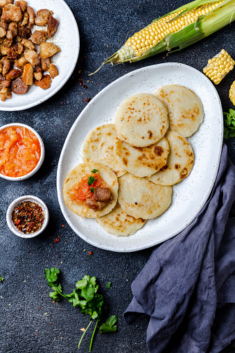 COLOMBIAN FOOD. Maize AREPAS and fried pork chicharron ans colombian tomato sauce. Top view. Black background.