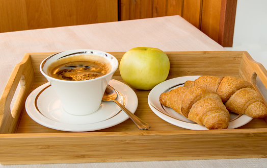 Traditional continental Breakfast with espresso coffee, croissants and an Apple on a wooden tray.