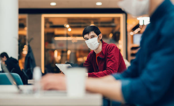cafe patrons in protective masks working on their laptops