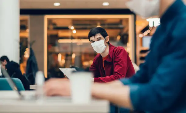 Photo of cafe patrons in protective masks working on their laptops