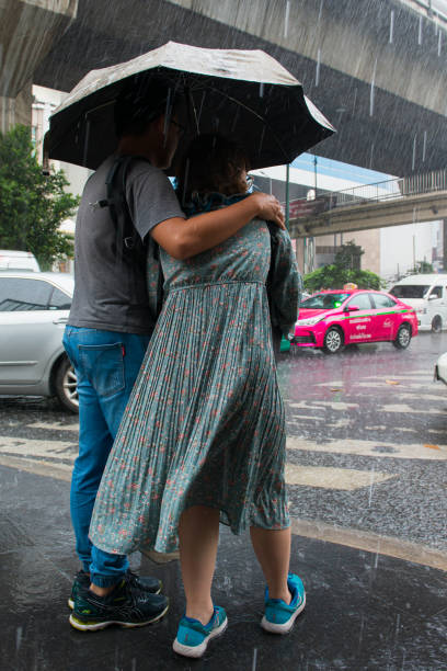 傘を持つ大雨のカップルは、道路を横断しようとします - wet dress rain clothing ストックフォトと画像