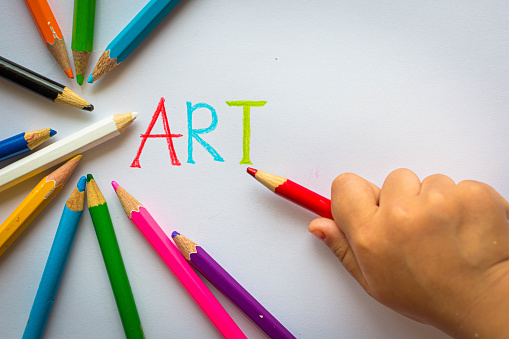 A little kid writing the word art on a white paper and with color stencils displayed around it. copy space.