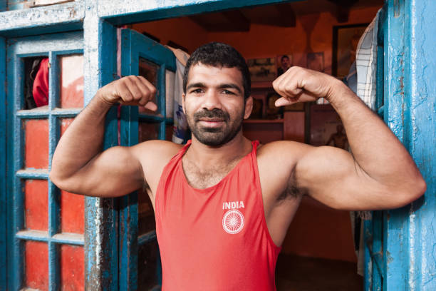Indian Wrestler Showing Muscles New Delhi India Indian Wrestler posing at the entrance of training and fitness room - cabin in downtown New Delhi. New Delhi, India. The India Logo on his shirt is a generic part of the Indian National Flag. greco stock pictures, royalty-free photos & images