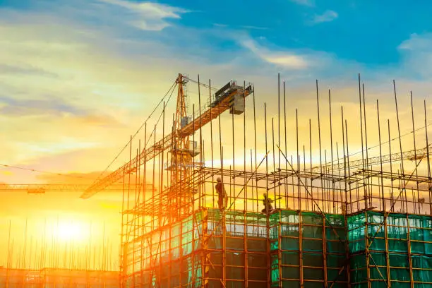 Photo of Tower crane and building construction site silhouette at sunrise.