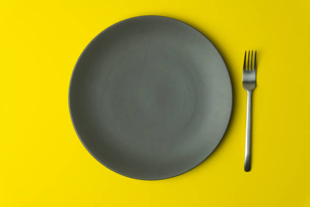 istock Empty plate on a yellow background. Empty gray ceramic plate with fork for food and dinner on a colored yellow background. 1226876111