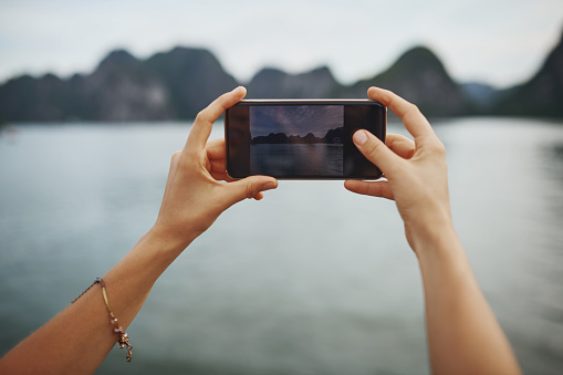 Shot of a young woman taking pictures of a river in Vietnam with her smartphone