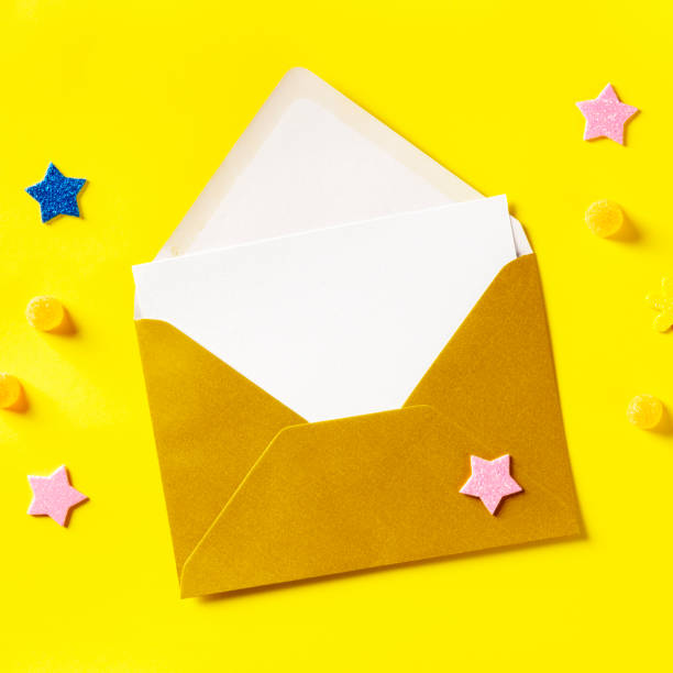 istock A white greeting card in a golden envelope, overhead square shot on a yellow background with glitter stars 1226879178