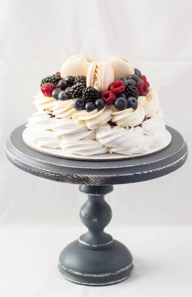 istock Pavlova cake with meringue, whipped cream adn fresh berries. Decorated with vanilla macaroons. Plain background. 1226879197