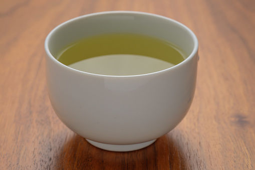 White pot of green tea on wooden table close-up