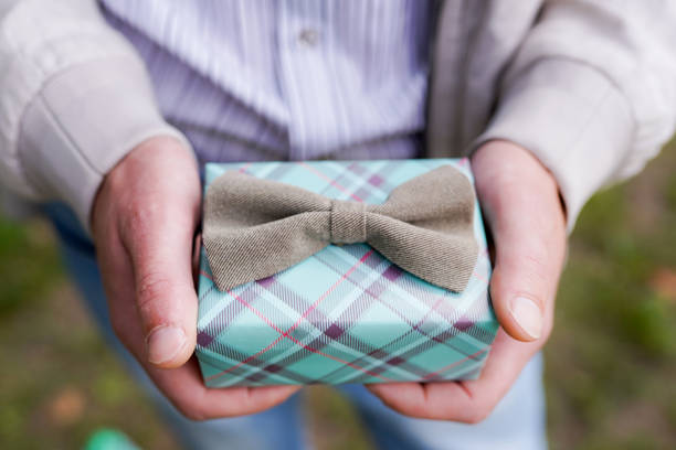 Chest view of an unrecognizable man wearing a suit who is about to give a gray gift box out of his jacket. The gray gift box is wrapped with blue ribbon.  Mother’s day / Valentine’s day / Promotion concept.