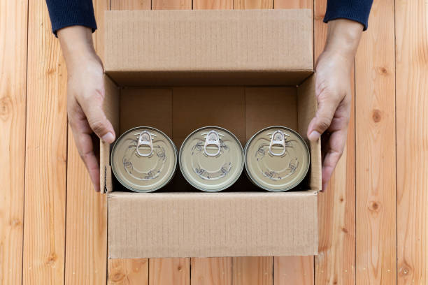 manos females sosteniendo una caja de cartón que contiene un alimento enlatado. - tuna chunks fotografías e imágenes de stock