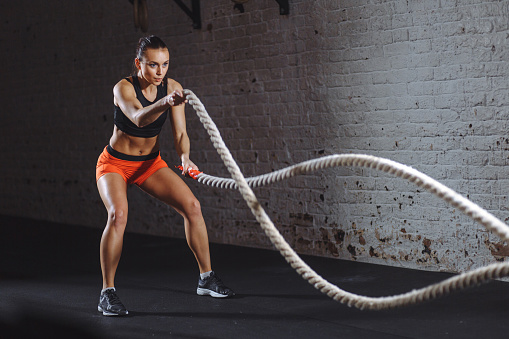 Woman training with battle rope in gym gym