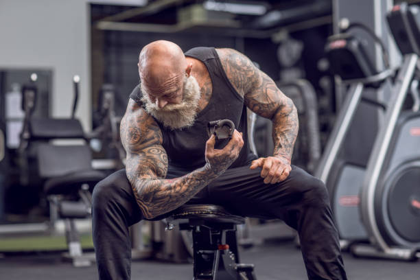 Tattooed Senior Man During Gym Workout Bearded Aggressive Senior Man during workout in a gym senior bodybuilders stock pictures, royalty-free photos & images
