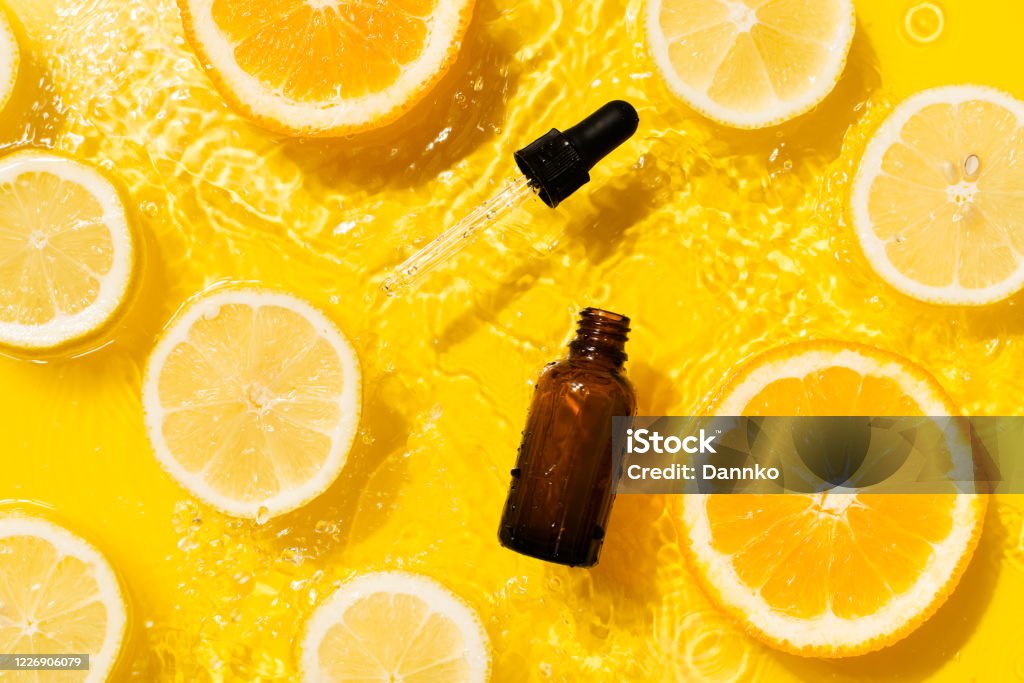 Cosmetic bottle product serum vitamin C with orange and lemon flat lay on yellow background clean water splashing Cosmetic bottle product serum vitamin C with orange and lemon flat lay on yellow background clean water splashing, top view, copy space Vitamin C Stock Photo