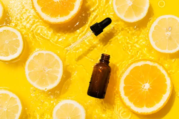 Photo of Cosmetic bottle product serum vitamin C with orange and lemon flat lay on yellow background clean water splashing