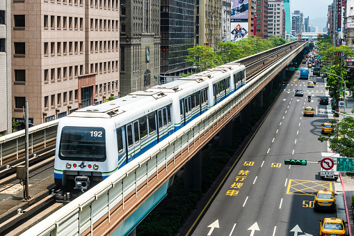 Taipei, Taiwan- May 5, 2020: Wenhu or Brown line of Taipei Metro in Taipei, Taiwan. View of a train traveling on elevated rails of Taipei Metro System between office towers under the blue clear sky.