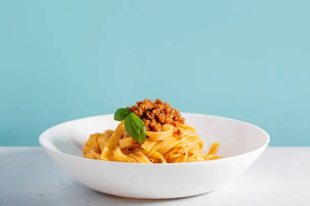 Italian pasta tagliatelle with traditional homemade meat sauce (4 hours of cooking) -  bolognese sauce. Light blue background.