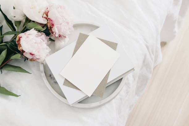 istock Wedding still life scene. Greeting card mockup scene, craft paper envelope, book on marble tray. Pink peony flowers on white linen table cloth. Vintage feminine styled photo, wooden floor. Flat lay. 1226918607
