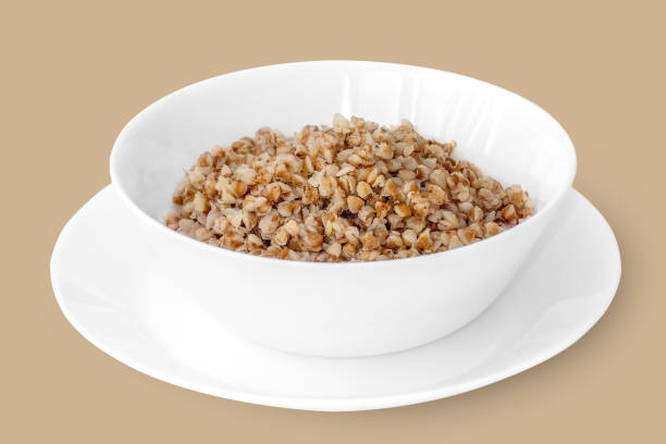istock Deep white plate with boiled buckwheat on a white saucer. Isolate on a beige background. Close-up. 1226921479