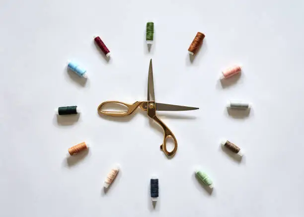 Flat lay picture of sewing accessories in the form of clock with arrows, isolated on white background. Scissors and colorful threads, ready for handmade usage.
