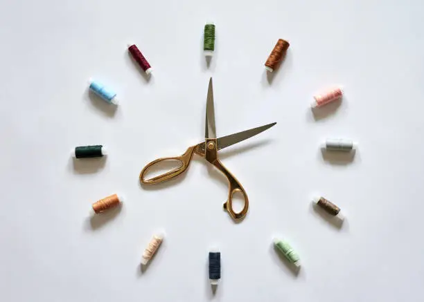 Flat lay picture of sewing accessories in the form of clock with arrows, isolated on white background. Scissors and colorful threads, ready for handmade usage.