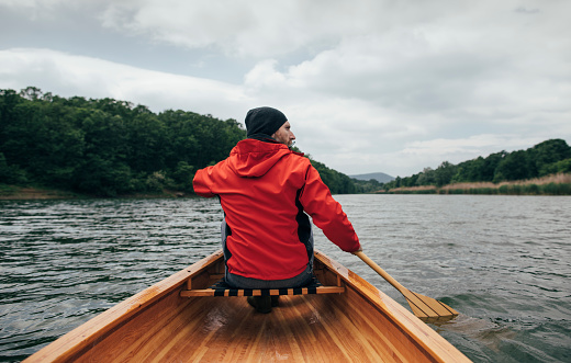 Rear view of man paddling canoe on the lake. Rainy day boat ride.