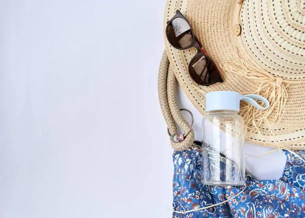 Flat lay picture of summer vacation beach accessories, isolated on white background. Beach bag, sunglasses, bottle of water with Be happy sign and straw hat. Tropical vacation planning.