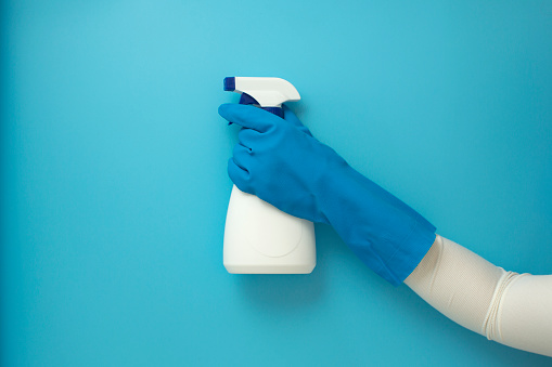 Flat lay women hand with blue protective glove, spraying to disinfect or cleaning on blue background.
