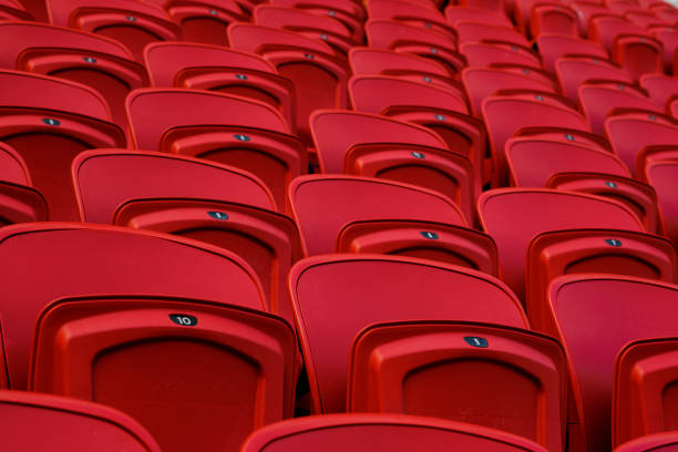 istock Empty red plastic seats in an empty stadium. Many empty seats for spectators in the stands. Empty plastic chairs seats for football fans. 1226954720