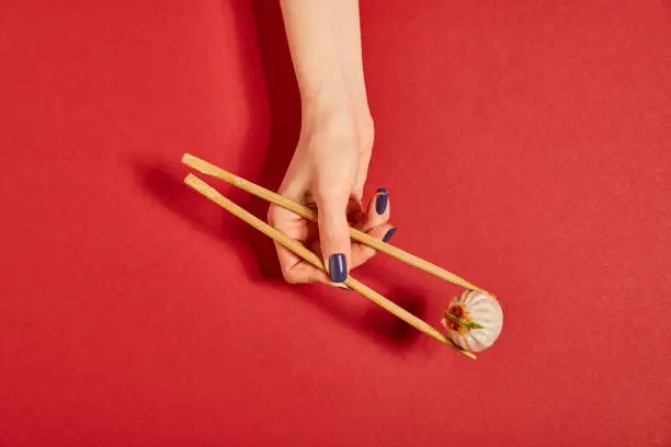 top view of woman holding chopsticks with steamed bun on red