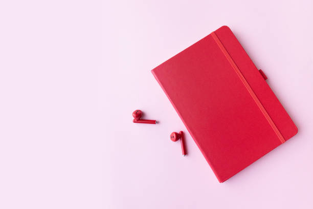istock Red notebook with wireless headphones on pink background with copy space. Minimal business concept 1226955316