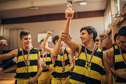 Group of boys, teenage boys basketball team celebrating wining a trophy.