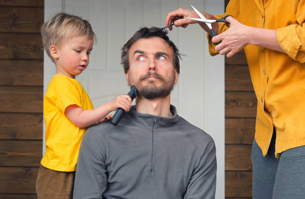 Family haircut at home during quarantine lockdown when closed all hairdressers. Mother cutting hair to father and little child boy cut dad beard with clipper. Beauty and selfcare at home lifestyle. Family haircut at home during quarantine lockdown when closed all hairdressers. Mother cutting hair to father and little child boy cut dad beard with clipper. Beauty and selfcare at home lifestyle. groom human role photos stock pictures, royalty-free photos & images