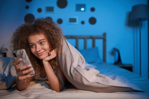 istock Smiling Young Woman Using Smartphone in Bed 1226961650