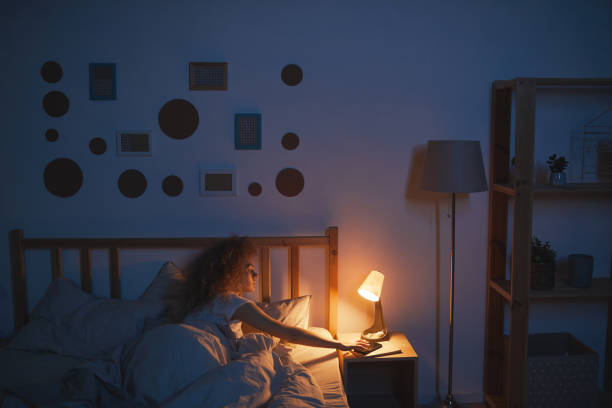 Young Woman Switching off Lamp at Night Wide angle portrait of curly-haired young woman lying in bed and switching off bedside lamp while preparing to sleep, copy space bedtime stock pictures, royalty-free photos & images