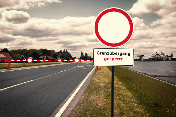 コンテナポートの前に交差する国境、背景には都市のシルエット。交通標識の碑文:"グレンツベルガング・ゲスペルト"。 - national border ストックフォトと画像