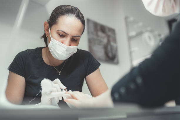 Professional manicure master dressed black in safety face mask using Electric Nail Polisher Tool for Glazing treatment manicure procedure. Small business everyday working concept. maestro profesional de manicura vestido negro con máscara facial de seguridad usando herramienta de pulidor de uñas eléctrica para el procedimiento de manicura de tratamiento de acristalamiento. concepto de trabajo diario de pequeñas empresas.