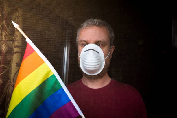 istock LGBT man self-isolating at home with face mask and rainbow flag 1226975868