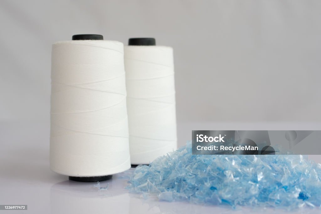 Bottle flake & Raw White Polyester FDY Yarn spool Bottle flake,PET bottle flake,Plastic bottle crushed,Small pieces of cut blue plastic bottles & Raw White Polyester FDY Yarn spool with white background Recycling Stock Photo