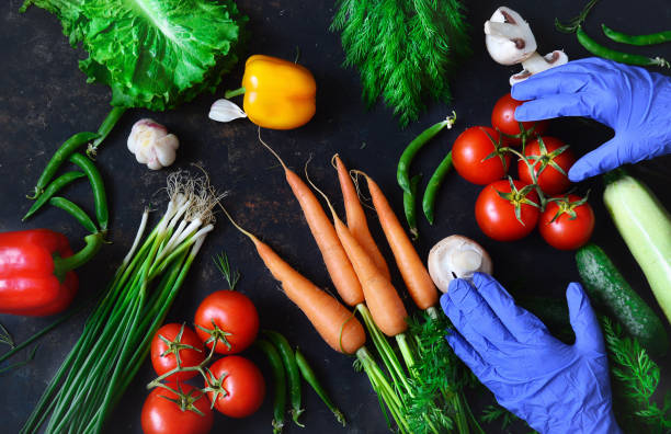 Healthy food concept with fresh vegetables and gloved hands on a dark background: tomato, zucchini, onion, lettuce, dill, pepper, cucumber, garlic, carrots. Coronavirus food delivery, food donation. Top view with copy space concepto de comida saludable con verduras frescas y manos enguantadas sobre un fondo oscuro: tomate, calabacín, cebolla, lechuga, eneldo, pimienta, pepino, ajo, zanahorias. entrega de alimentos coronavirus, donación de alimentos. vista superior con espac