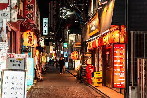 Tokyo, Japan - April 3, 2019: Shinjuku ward downtown with narrow alley lane street with izakaya restaurants at night and signs near Okubo station