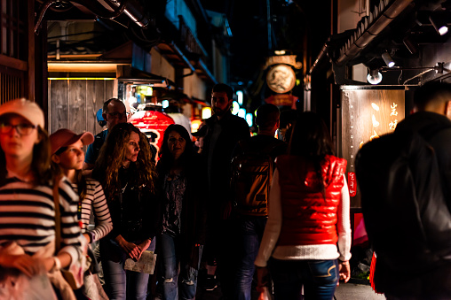 Kyoto, Japan - April 16, 2019: People crowd walking on narrow Pontocho alley district street at night by izakaya restaurants signs in dark evening