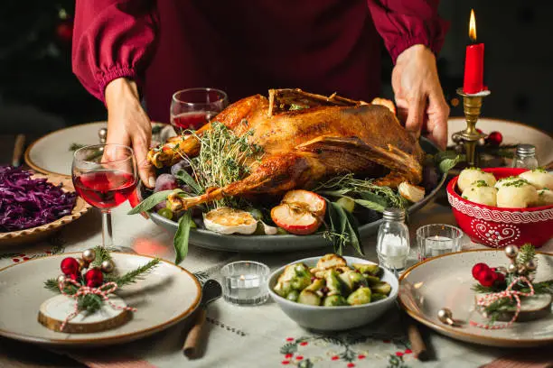 Close-up of woman's hands setting the table, serving roast duck for Christmas dinner.