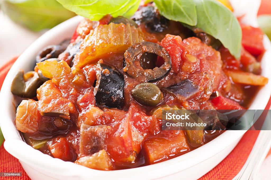 Caponata with olives in a white bowl Sicilian fried vegetable with olives and tomato sauce as closeup on a white bowl Antipasto Stock Photo