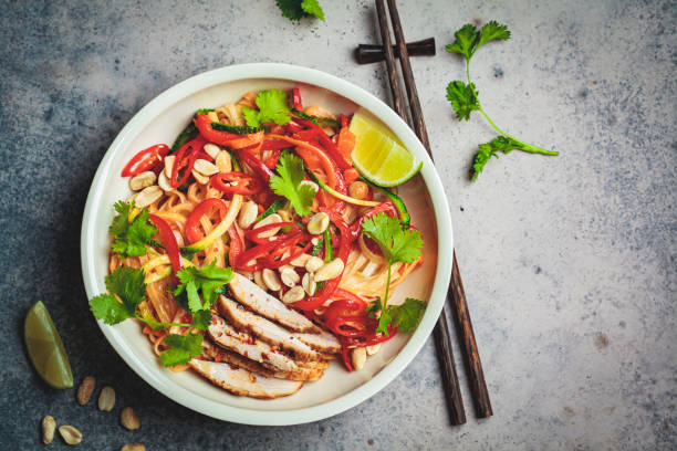 pad thai noodles with chicken, peanuts and vegetables in bowl, top view, dark background. - thailand thai culture thai cuisine pad thai imagens e fotografias de stock