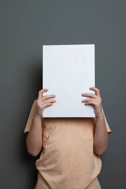 istock Cute boy is holding a blank page in front of his head 1226991323