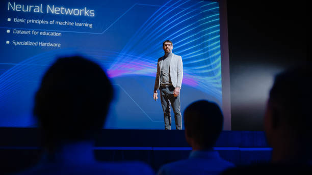 istock On Stage Speaker Does Presentation of New Product, Uses Remote Control for Presentation, Showing Infographics, Statistics Animation on Big Screen. Live Event / Device Start-up Release 1226991343